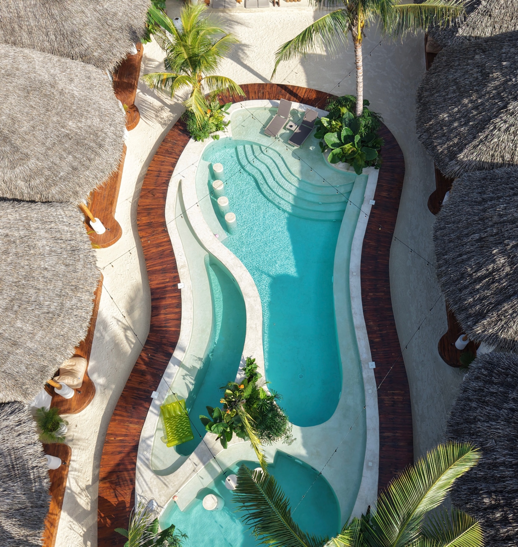 Aerial view of the curved main pool at Kai Zanzibar between thatched roofs and palms