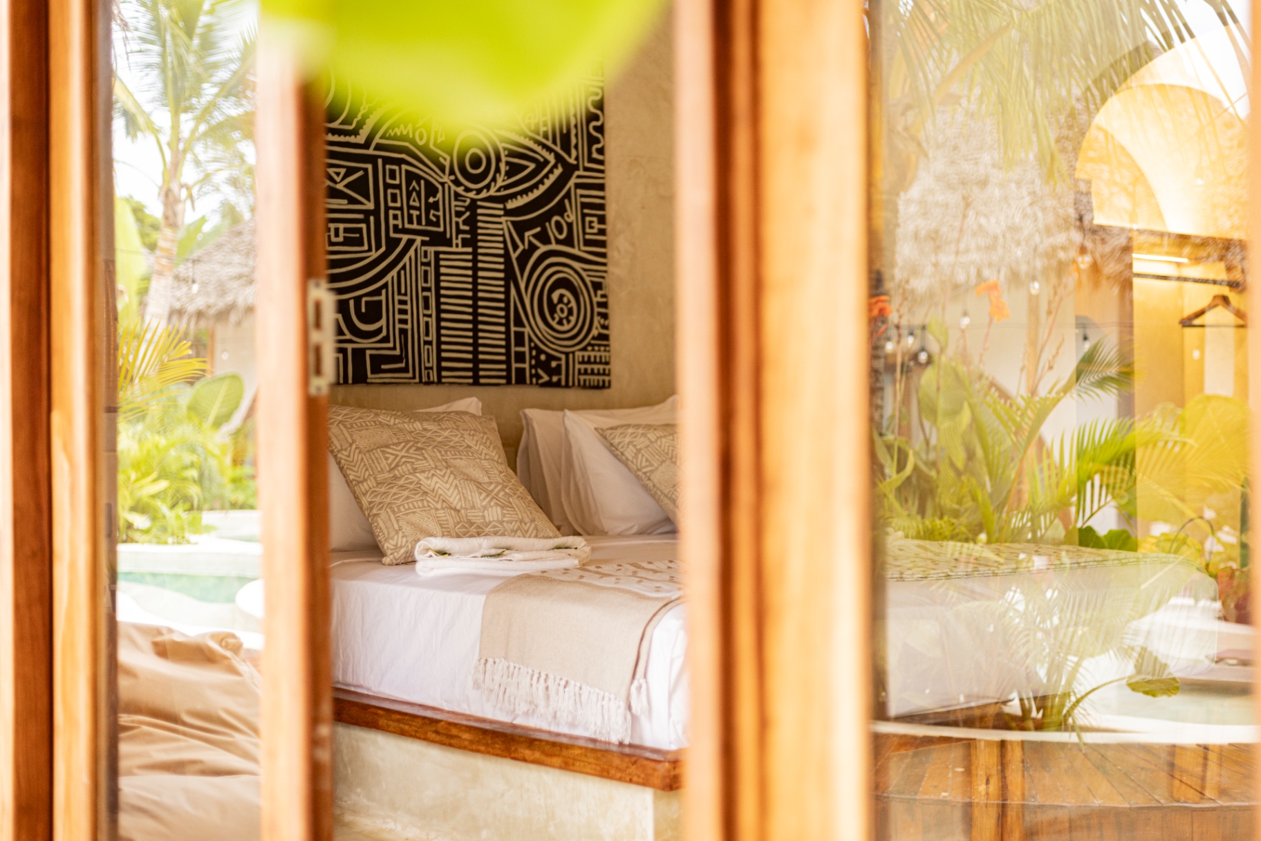 View through timber doors into a villa bedroom framed by palms