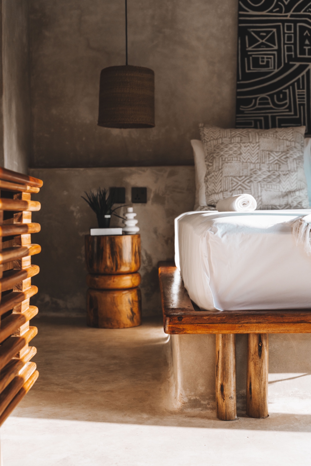 Carved timber stump bedside table and rattan pendant beside a platform bed
