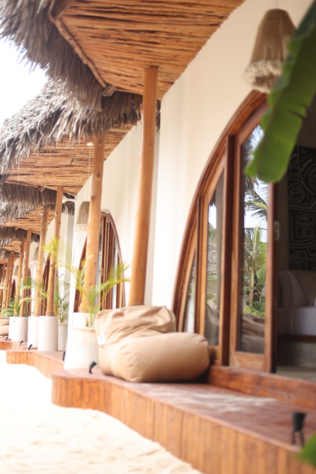 Row of thatched villa verandas with arched timber doors above a sand terrace